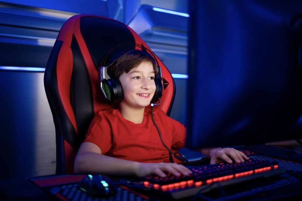 small boy with a red shirt and headphones playing on a gaming PC